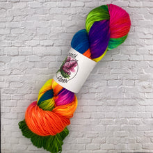 Load image into Gallery viewer, Colorful skein of yarn with a label on a white brick background