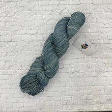 Load image into Gallery viewer, Blue skein of yarn with a label on a white brick background