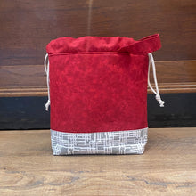 Load image into Gallery viewer, A drawstring project bag with a multicolored geometric pattern and a gray denim-like material, featuring a wrist strap handle.