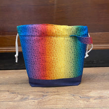 Load image into Gallery viewer, A drawstring project bag with a multicolored geometric pattern and a gray denim-like material, featuring a wrist strap handle.
