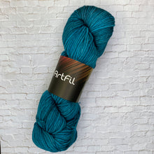 Load image into Gallery viewer, Blue skein of yarn with 'Artfil' label on a light brick wall background