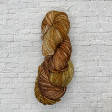 Load image into Gallery viewer, Multicolored skein of yarn against a light gray brick wall.