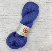 Load image into Gallery viewer, Blue skein of yarn with a label on a white brick background

