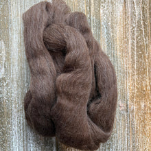 Load image into Gallery viewer, A bundle of dark brown wool roving or fiber placed on a rustic whitewashed wooden surface.
