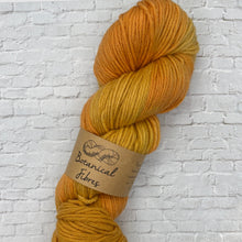Load image into Gallery viewer, Mustard yellow skein of yarn with a label on a textured white background
