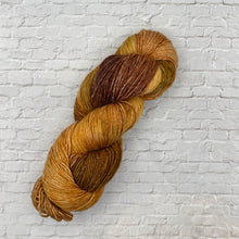 Load image into Gallery viewer, Brown and yellow skein of yarn on a light gray brick wall background
