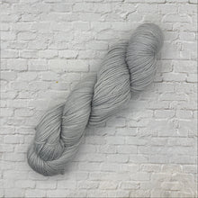 Load image into Gallery viewer, Gray skein of yarn against a light brick wall

