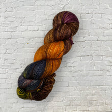 Load image into Gallery viewer, Multicolored skein of yarn on a white brick wall background
