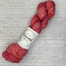 Load image into Gallery viewer, Red skein of yarn with a label on a white brick background
