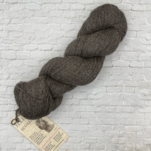 Load image into Gallery viewer, Gray skein of yarn with a label on a light gray brick background
