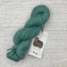 Load image into Gallery viewer, Green skein of yarn with a label on a light brick wall background
