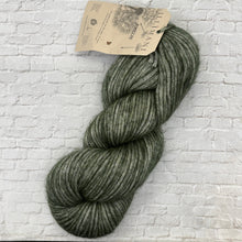 Load image into Gallery viewer, Green skein of yarn with a label on a white brick background

