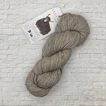 Load image into Gallery viewer, Gray skein of yarn with a label on a light brick background
