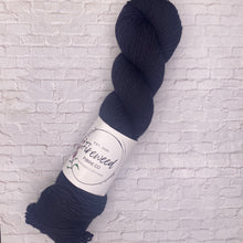 Load image into Gallery viewer, Navy skein of yarn with a label on a white brick background
