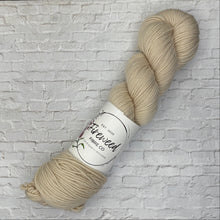 Load image into Gallery viewer, Beige skein of yarn with a label on a white brick background
