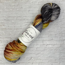 Load image into Gallery viewer, Multicolored skein of yarn with a label on a light gray brick background
