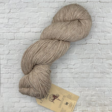 Load image into Gallery viewer, Beige skein of yarn with a label on a light brick wall background
