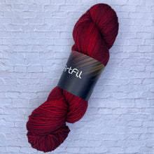 Load image into Gallery viewer, Red skein of yarn with a label on a textured white background
