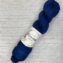 Load image into Gallery viewer, Blue skein of yarn with a label on a white brick background
