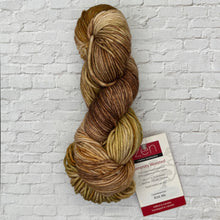 Load image into Gallery viewer, Skein of brown yarn with a label on a white brick wall background
